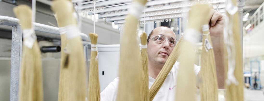 An Evonik employee in Schörfling, Austria, hangs bundled SEPURAN® membrane fibers on a frame. The fibers are used for gas treatment.