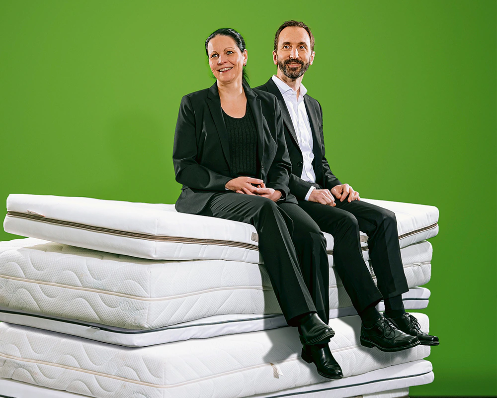 Chemikerin Annegret Terheiden und Chemiker Michael Ferenz von Evonik sitzen auf einem Matratzenstapel.